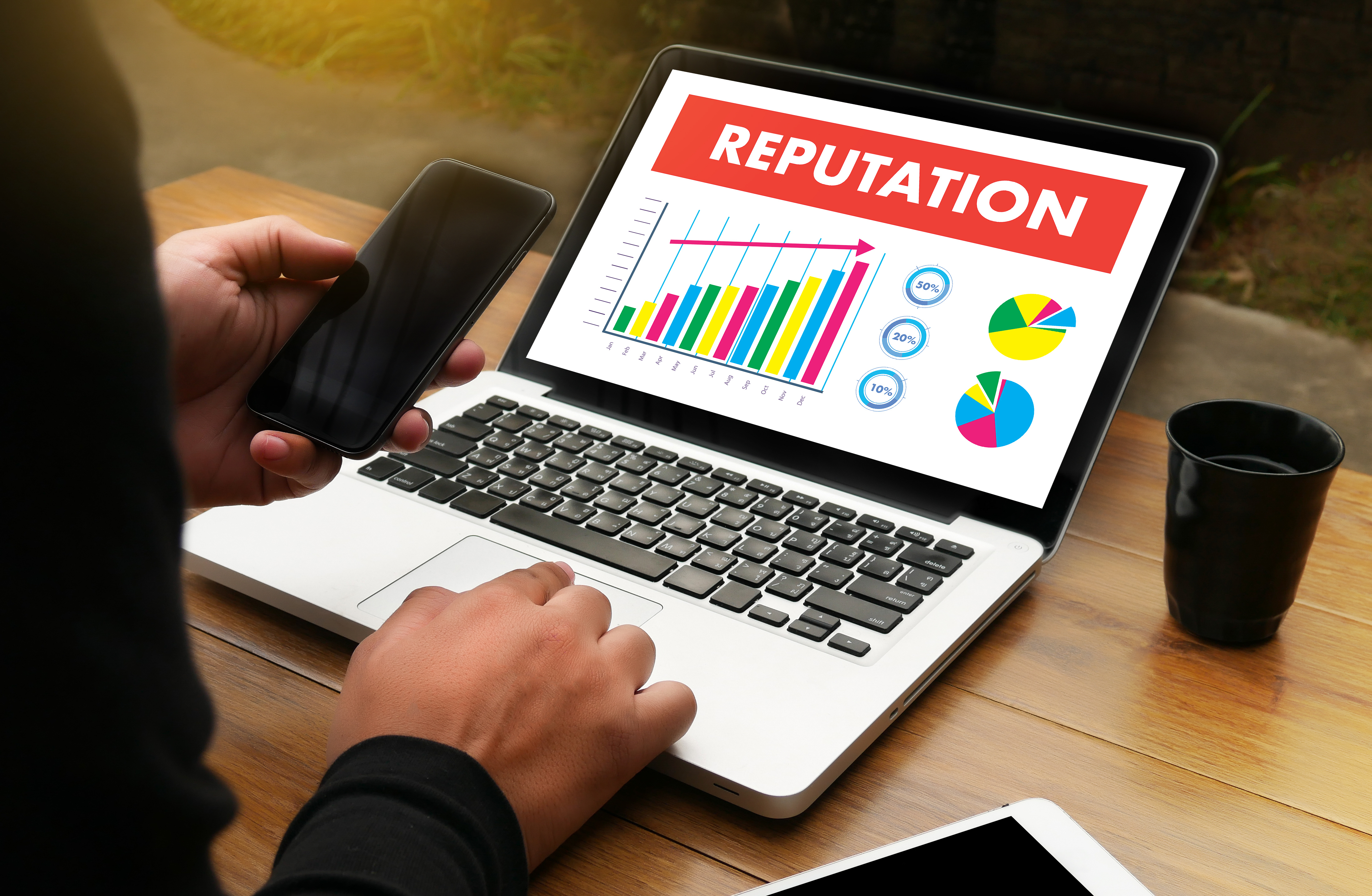 a businessman on his phone, with a laptop portraying the label 'Reputation' alongside some graphs